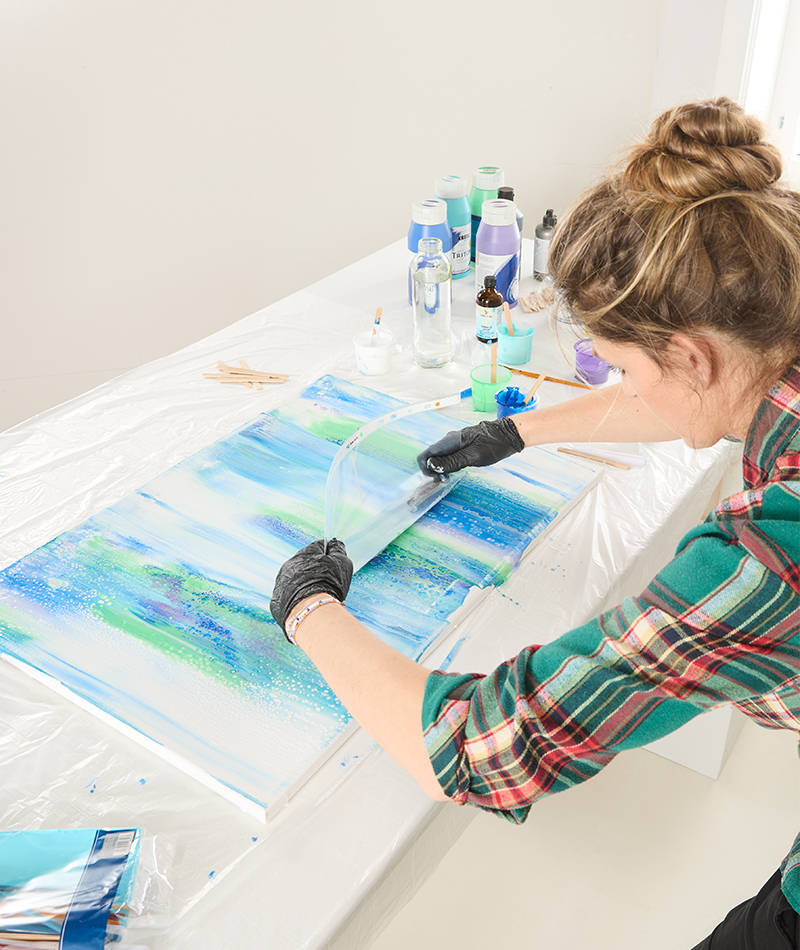 Mit Hilfe einer Folie wird die Farbe über die Leinwand gezogen